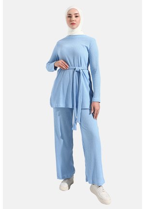 Light blue ribbed two-piece outfit featuring a long top with a tie belt and matching wide-leg pants, paired with white sneakers.