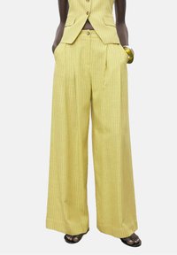 Pantalones de pierna ancha a rayas amarillas con cintura alta y bolsillos laterales, confeccionados en una tela texturizada. Combinados con una chaqueta a juego.