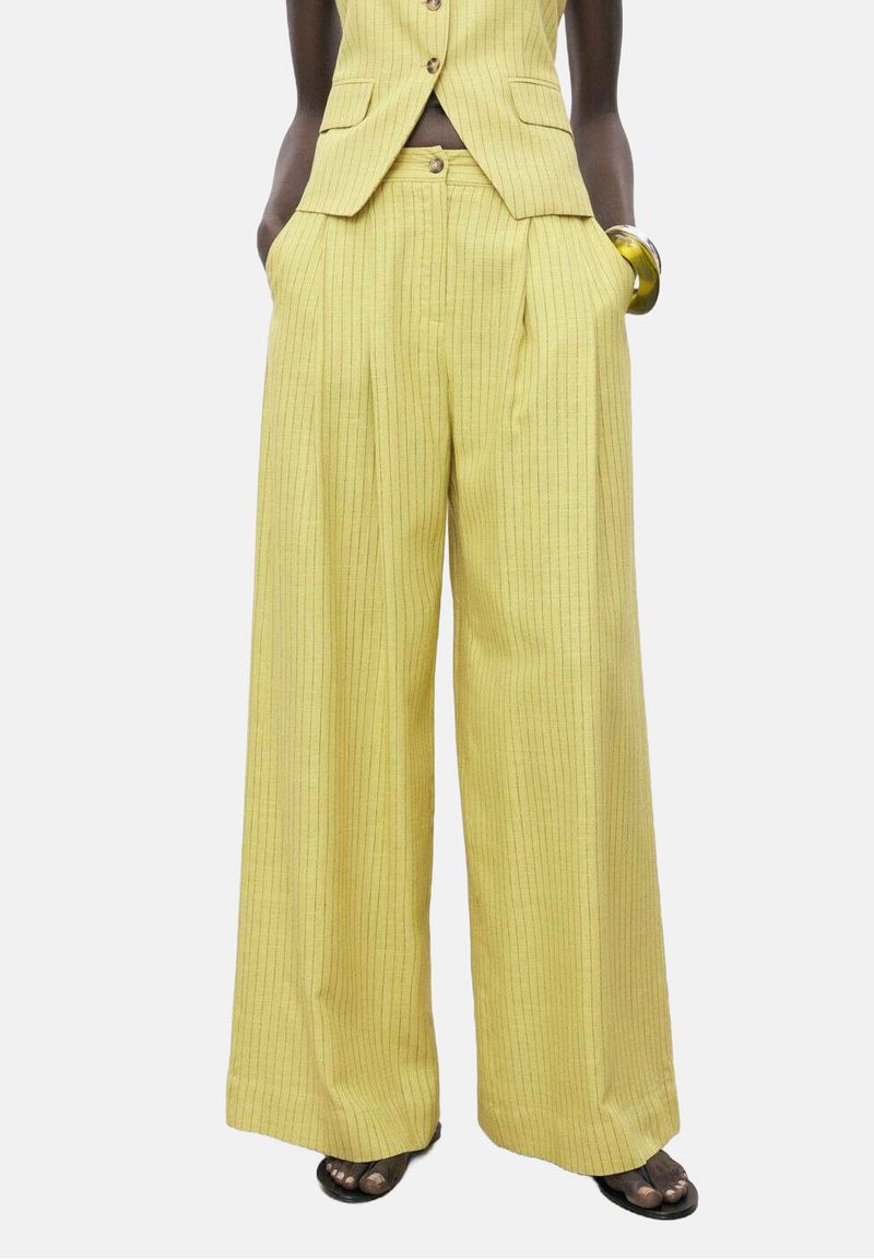 Pantalones de pierna ancha a rayas amarillas con cintura alta y bolsillos laterales, confeccionados en una tela texturizada. Combinados con una chaqueta a juego.