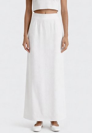 Donna che indossa una gonna bianca a vita alta lunga fino alle caviglie con tasche laterali e ballerine bianche, su uno sfondo bianco uniforme.