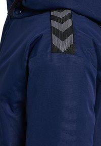 Navy blauwe stoffen broek met een gestructureerd oppervlak, voorzien van een zwart en reflecterende chevronpatroon band aan de zijkant voor extra detail.