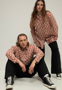 Camisas de manga larga de colores marrón y blanco con un patrón, en dos modelos, combinadas con pantalones negros y zapatillas altas. Diseño plano, ajuste relajado.