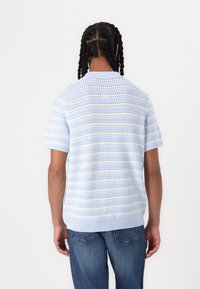 Lys blå strikket kortærmet sweater med vandrette striber og åbne mønstre. Ribbet halsudskæring og kant tilføjer tekstur til designet.