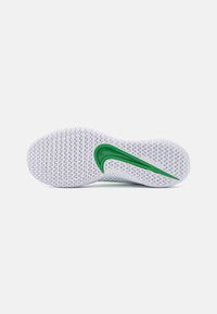 Bílá podrážka tenisky s texturovaným gripem, s akcentem zeleného loga Nike. Čistý design s zaoblenými okraji, lehký materiál.
