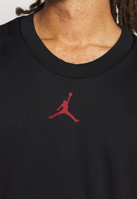 Černé bavlněné tričko s kulatým výstřihem, na přední straně s červeným logem Jumpman. Hladká textura, volný střih.
