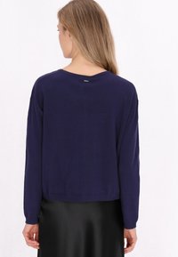 Pulover scurt de culoare bleumarin, cu mâneci lungi, textură moale și decolteu rotund. Prezintă o etichetă mică cusută pe spate.