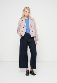 Ανοιχτό ροζ σακάκι με διπλό στήθος και μαύρα κουμπιά, μπλε τοπ, φαρδιά σκουρόχρωμη τζιν παντελόνια και μαύρα γυαλιστερά μποτάκια αστραγάλου.