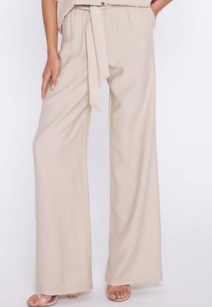 Beżowe, szerokie spodnie z wysokim stanem z dopasowanym paskiem z tkaniny zawiązanym w talii, noszone z przezroczystymi, odkrytymi na palce szpilkami.
