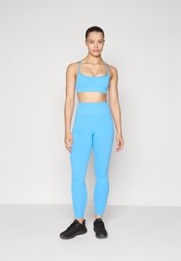 Sutiã desportivo azul claro e leggings de cintura alta feitos de tecido suave, combinados com ténis desportivos pretos.