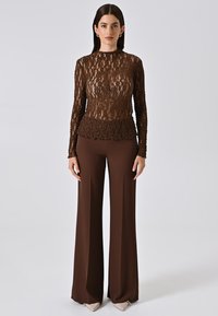 Top lungo a maniche lunghe in pizzo marrone con corpetto aderente e orlo peplum abbinato a pantaloni larghi marroni a vita alta e décolleté beige a punta.