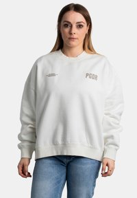 Felpa bianca con vestibilità oversize, colletto a coste e maniche a cuffia. Presenta testo grigio chiaro: "PGDR" e "Tutto ciò che abbiamo."