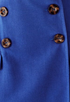 Sininen kangas vaatteessa, jossa on kaksirivinen suunnittelu, kahdella ruskealla napilla ja hienoilla ommeltyyppisillä yksityiskohdilla. Sileä pinta ja elinvoimainen väri.