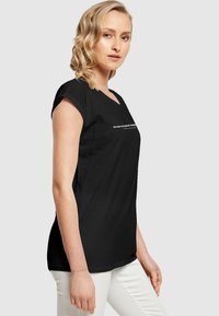 Sort kortærmet t-shirt med v-hals og hvid tekst, der står "DU HAR MAGTEN TIL AT FORANDRE" på forsiden.