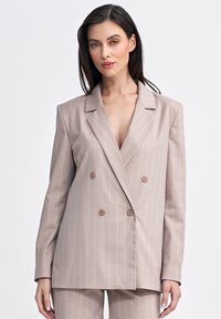 Jasno beżowa marynarka dwurzędowa z białymi pionowymi paskami, z klapami ze ścięciem i brązowymi guzikami, o luźnym kroju i gładkiej fakturze.