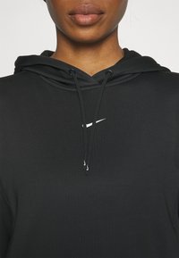 Felpa nera con cappuccio realizzata in tessuto morbido, caratterizzata da un logo Nike bianco. Include cordini regolabili e una tasca a marsupio.