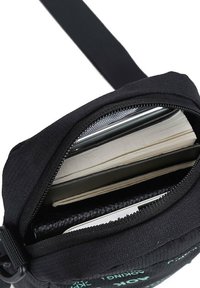 Pochette noire à fermeture éclair ouverte montrant un smartphone, un carnet et un portefeuille à l'intérieur.