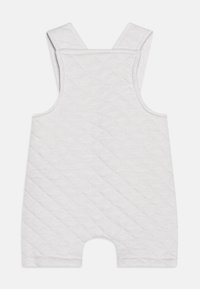 Biały pikowany romper z szerokimi ramiączkami, z wzorem w diamenty i otwartą nogawką. Miękka tekstura, bez widocznych elementów metalowych ani akcentów.