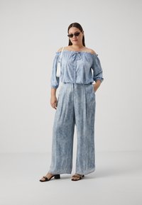 Svetlo modra bluzka off-shoulder z nabranim dekoltejem, v kombinaciji s širokimi hlačami, ki imajo podoben vzorec. Črne sandale dopolnjujejo videz.