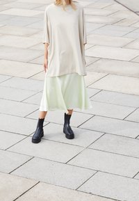 Beige oversized t-shirt with short sleeves, layered over a mint green midi skirt, paired with black ankle boots with thick soles.