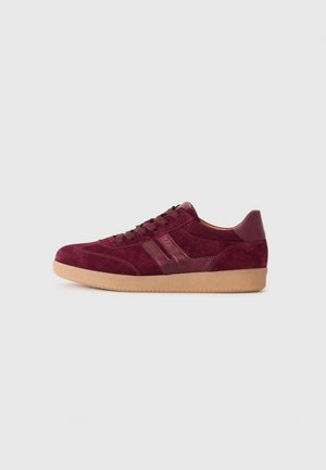 Bordeaux suède sneakers met bruine veters, twee glanzende zijstrepen en een lichtbruine rubberen zool, gezien vanaf de buitenkant.
