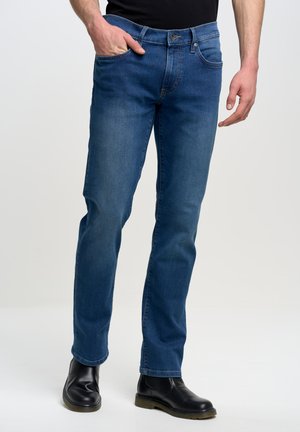 Jeans in denim blu con design a gamba dritta, dotati di tasca frontale, chiusura con bottone e abbinati a stivaletti neri.