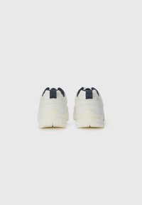 White athletic shoes with dark blue accents, featuring a textured rubber sole, padded collars, and pull tabs at the heel.
