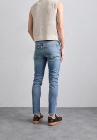 Ljusblå smala jeans med en blekt finish, kombinerade med en beige ärmlös stickad topp. Bruna sneakers med en texturerad sula och flerfärgade randen.