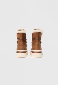 Bottines en cuir brun avec doublure en fausse fourrure, détails en dentelle et semelle couleur crème. La vue arrière met en avant la texture lisse et les accents.