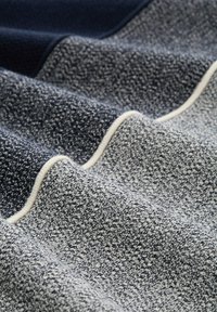 Strukturiertem Stoff in Marineblau und Hellgrau, mit einem gewebten Muster und cremefarbenem Rand. Das Material zeigt eine weiche, leicht erhabene Oberfläche.