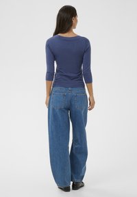 Haut bleu marine à manches longues avec un large décolleté, associé à un jean bleu clair à coupe ample avec des poches arrière, porté avec des bottes noires.