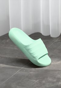Mint green slide sandal with a textured strap design and open toe. Made of soft material, featuring a smooth surface and slight curve.