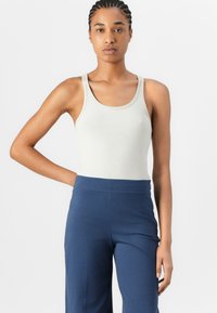 Débardeur côtelé en coton beige clair, avec un col arrondi et des bretelles larges, associé à un pantalon bleu marine taille haute.