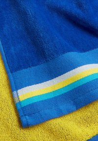 Asciugamano blu e giallo con una superficie texturizzata. La sezione blu presenta righe orizzontali in bianco, giallo e azzurro vicino al bordo.