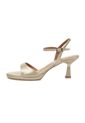 Sandalia dorada brillante con puntera abierta, tacón curvado de altura media y correa ajustable en el tobillo con hebilla sobre fondo blanco.