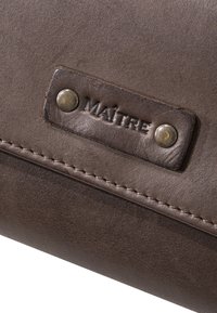 Brun læderpung med tekstureret overflade, præget "MAÎTRE" label og to metaltrykknapper. Detaljeret syning langs kanten.