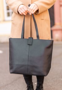 Zwarte leren schoudertas met een gladde textuur, rechthoekige vorm en lange handvatten. Beschikt over een centrale naad en een klepsluiting.