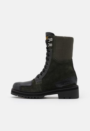 Botte de combat en daim vert foncé avec des accents en cuir noir, fermeture à lacets sur le devant, semelle épaisse en caoutchouc et col rembourré à la cheville.
