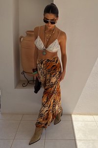 Bralette bianco scintillante, gonna maxi a stampa animale in arancione e nero, stivali con tacco verde oliva, collane sovrapposte, occhiali da sole e una borsa nera.