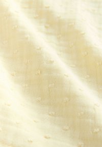 Textured light yellow fabric featuring small, raised dots, soft to the touch, with a slightly sheer and woven appearance.