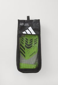 Gants de gardien Adidas Predator dans un sac en maille noire, comprenant des gants verts avec des rayures noires et un marquage, conçus pour l'entraînement au football.