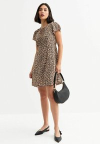 Abito a stampa floreale in beige con maniche a palloncino corte, scollo a goccia, abbinato a una borsa nera e a ballerine nere a punta.