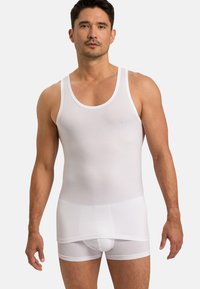 Bílý bavlněný top bez rukávů s širokými ramínky a přiléhavým střihem, spárovaný s bílými boxerky, vykazující hladkou texturu a minimální detaily.