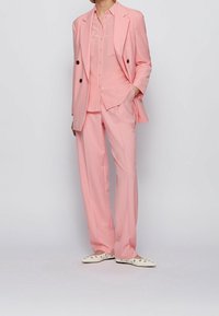 Světle růžový oblek s dvouřadým sako, košilí s knoflíky a kalhotami se širokými nohavicemi. Měkká tkanina s hladkým povrchem, zvýrazněná tmavými knoflíky.