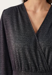 Svart metallisk topp med djup V-ringning och textil med subtil lyster. Samlad midjedetalj förhöjer designen.