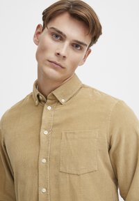 Button-up shirt in lichtbruine corduroy, met een kraag, een borstzak en witte knopen, met een ribbelstructuur.