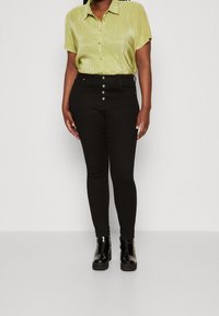 Grön kortärmad skjorta med krage och vertikala ränder, tillsammans med svarta höga byxor med metallknappdetaljer. Svarta klackboots.