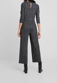 Mono de patrón negro y gris con mangas tres cuartos, piernas anchas y detalle en la espalda con abertura en forma de ojo de cerradura, hecho de una suave tela texturizada.