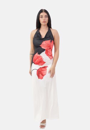 Femme portant une robe sans manches noire et blanche à imprimé floral rouge vif, se tenant devant un fond clair.
