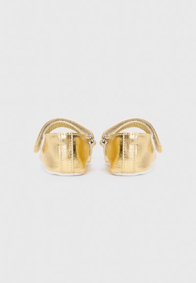 Zapatos de cuero dorado con un acabado metálico brillante, que cuentan con correas en el tobillo y una suela blanca suave. Diseño compacto y redondeado.