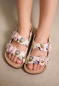 Sandales de style Birkenstock avec une base beige, arborant un motif floral et des imprimés de personnages Disney. Deux boucles roses réglables.
